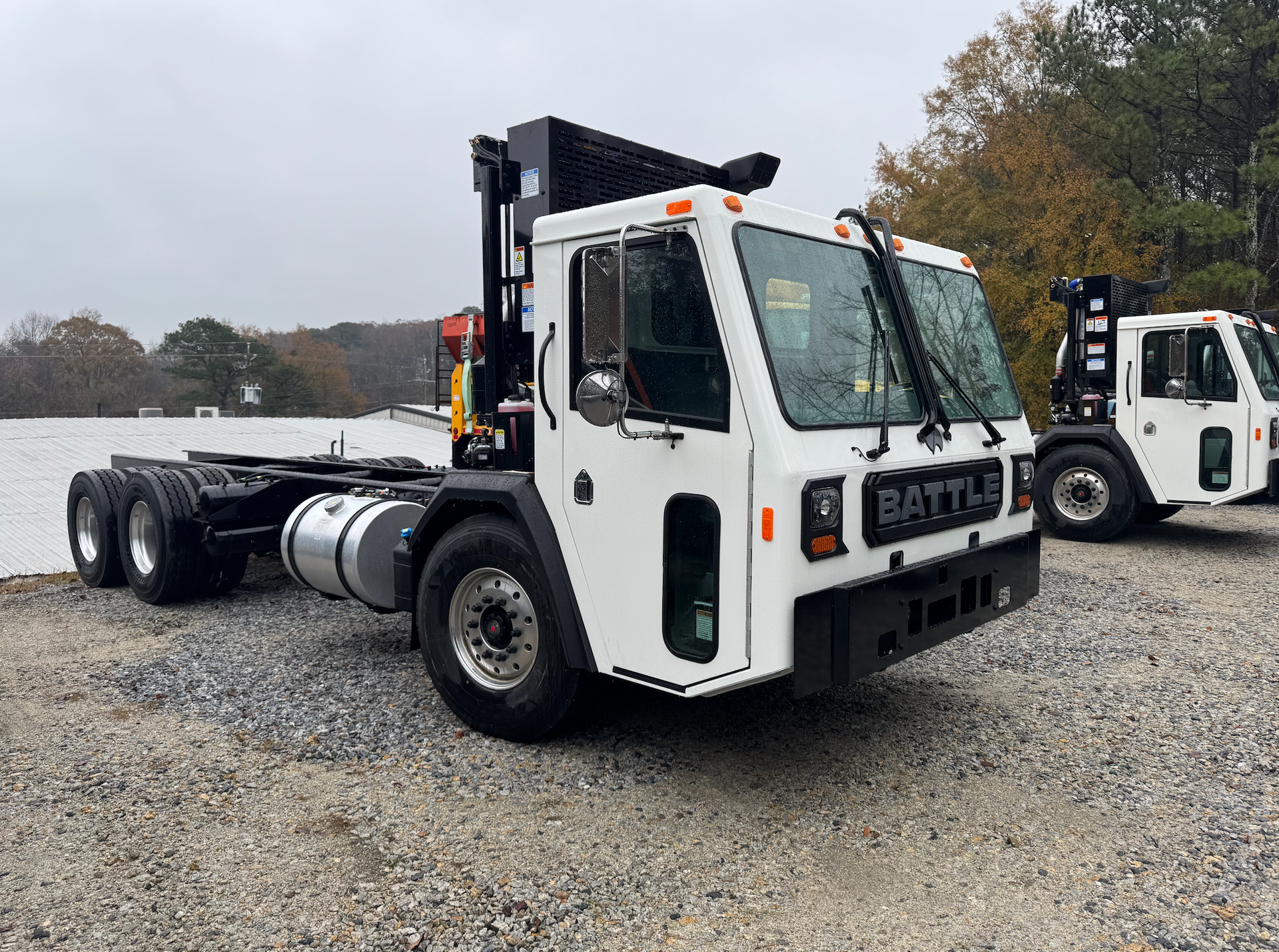 A white truck is parked in a gravel lot next to a forklift.
