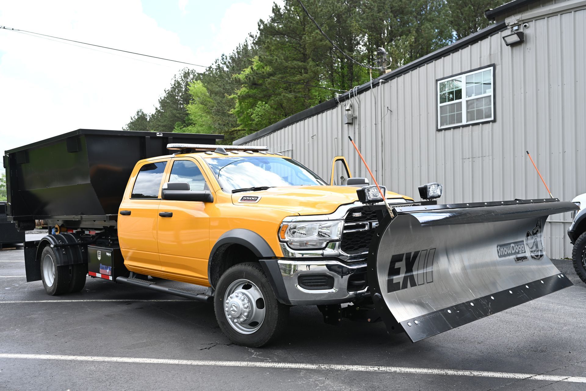 A yellow truck with a snow plow attached to it is parked in front of a building.