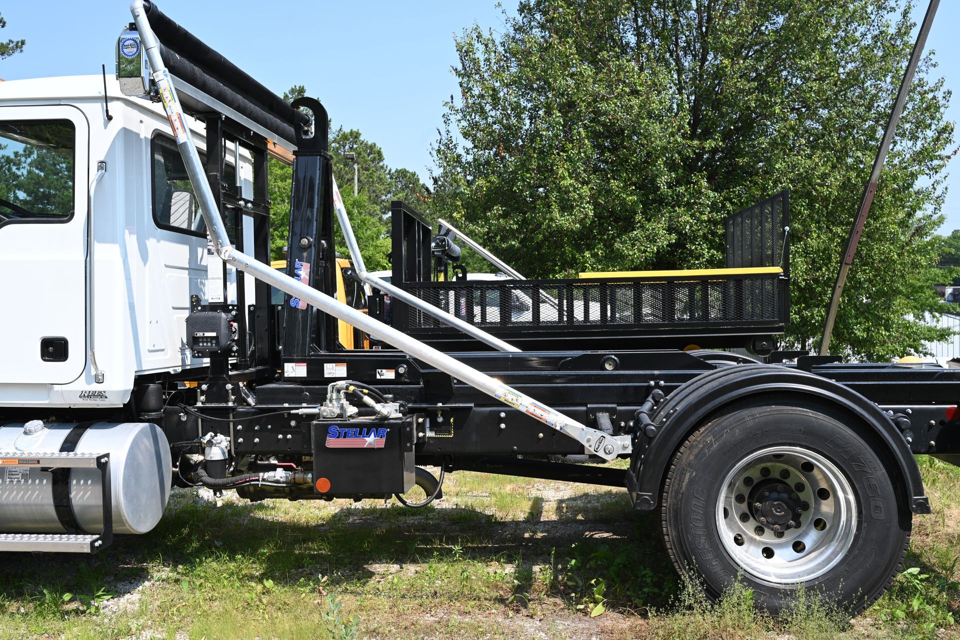 A dump truck is parked in a grassy field with trees in the background.