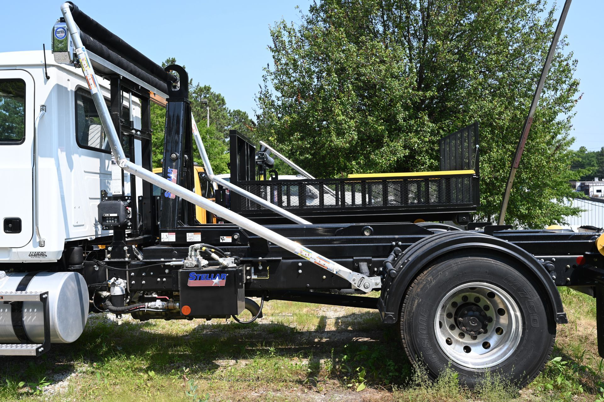 A dump truck is parked in a grassy field with trees in the background.