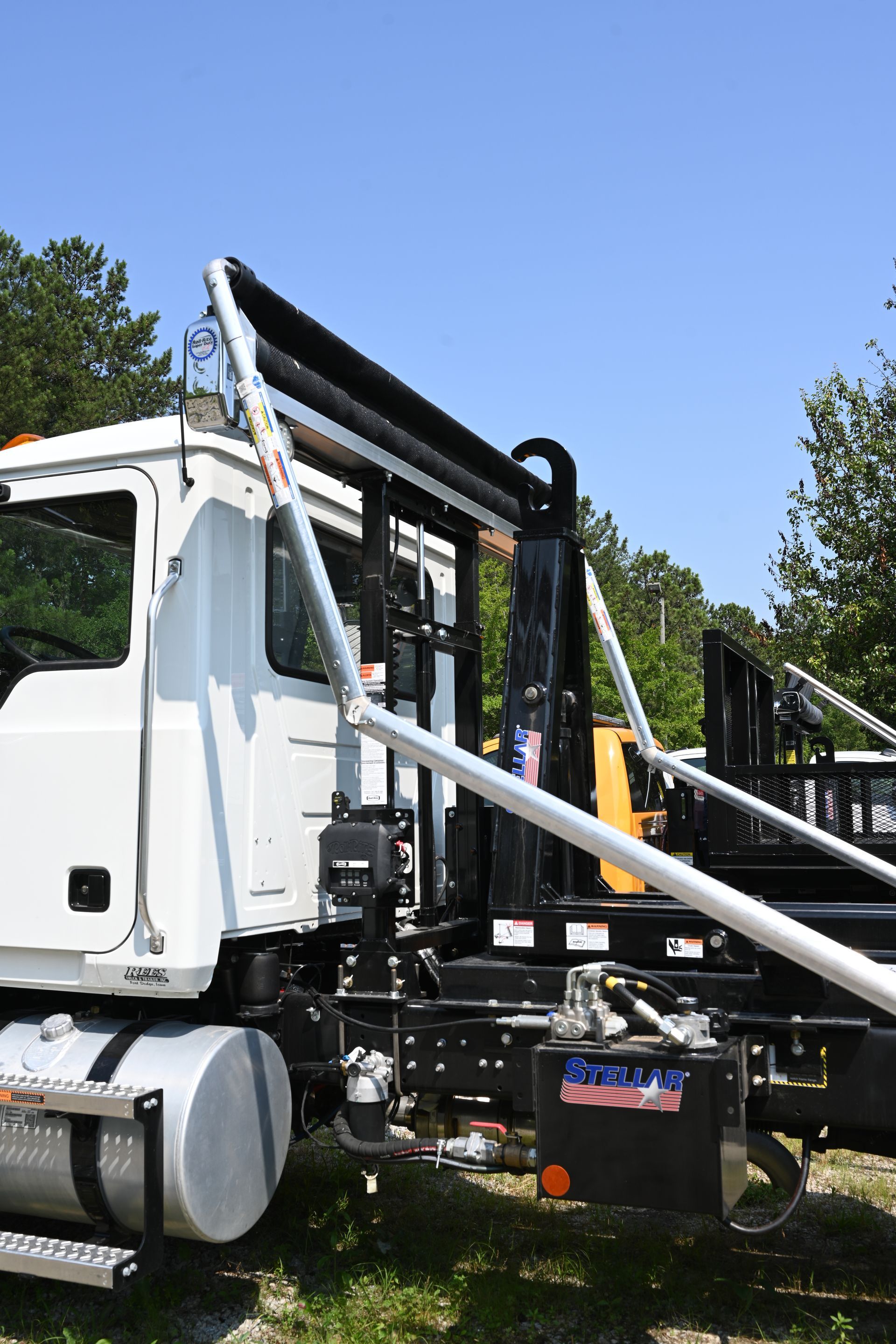 A white truck with a large pipe attached to it is parked in the grass.