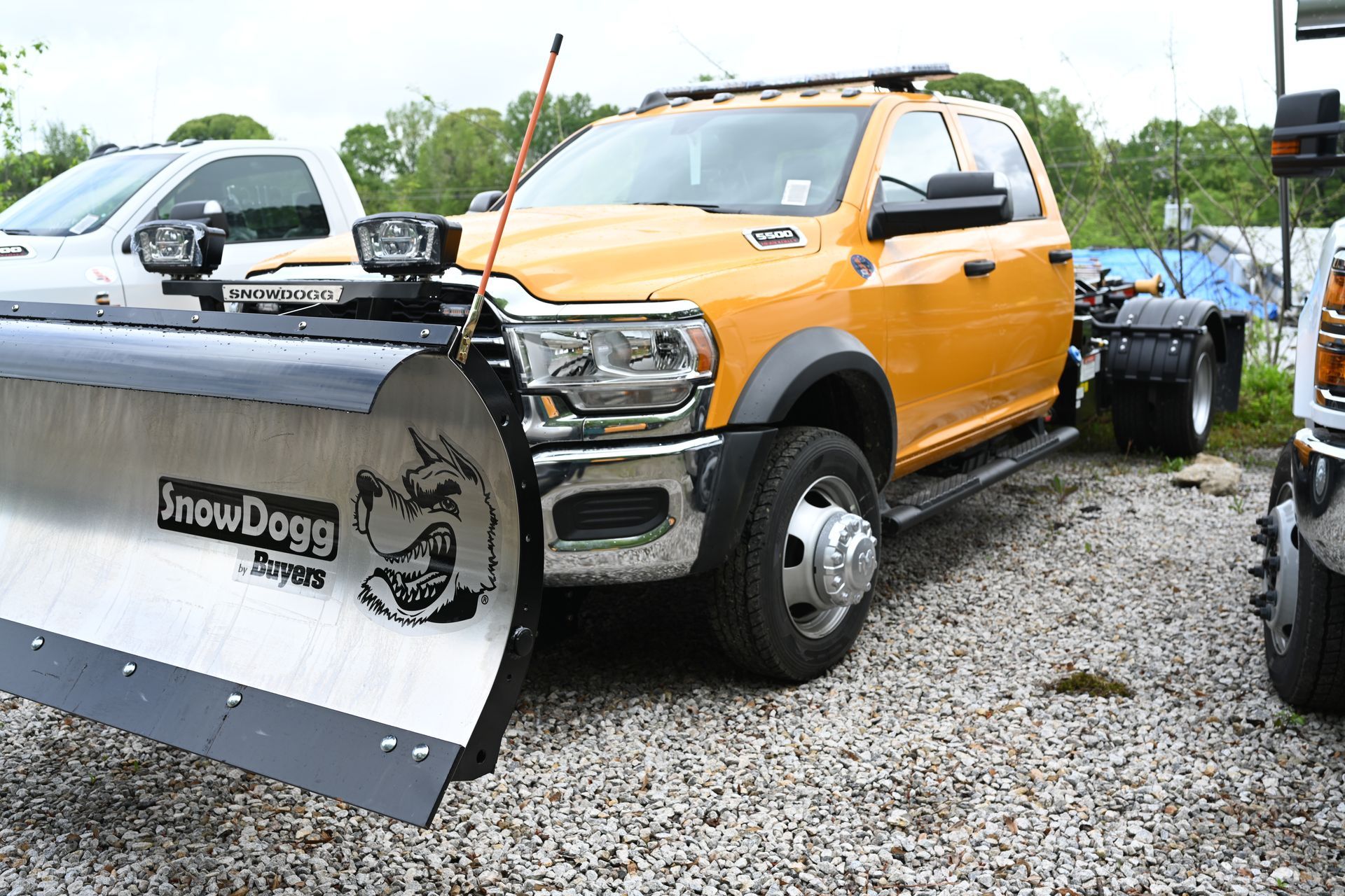 An orange truck with a snow plow attached to it is parked in a gravel lot.