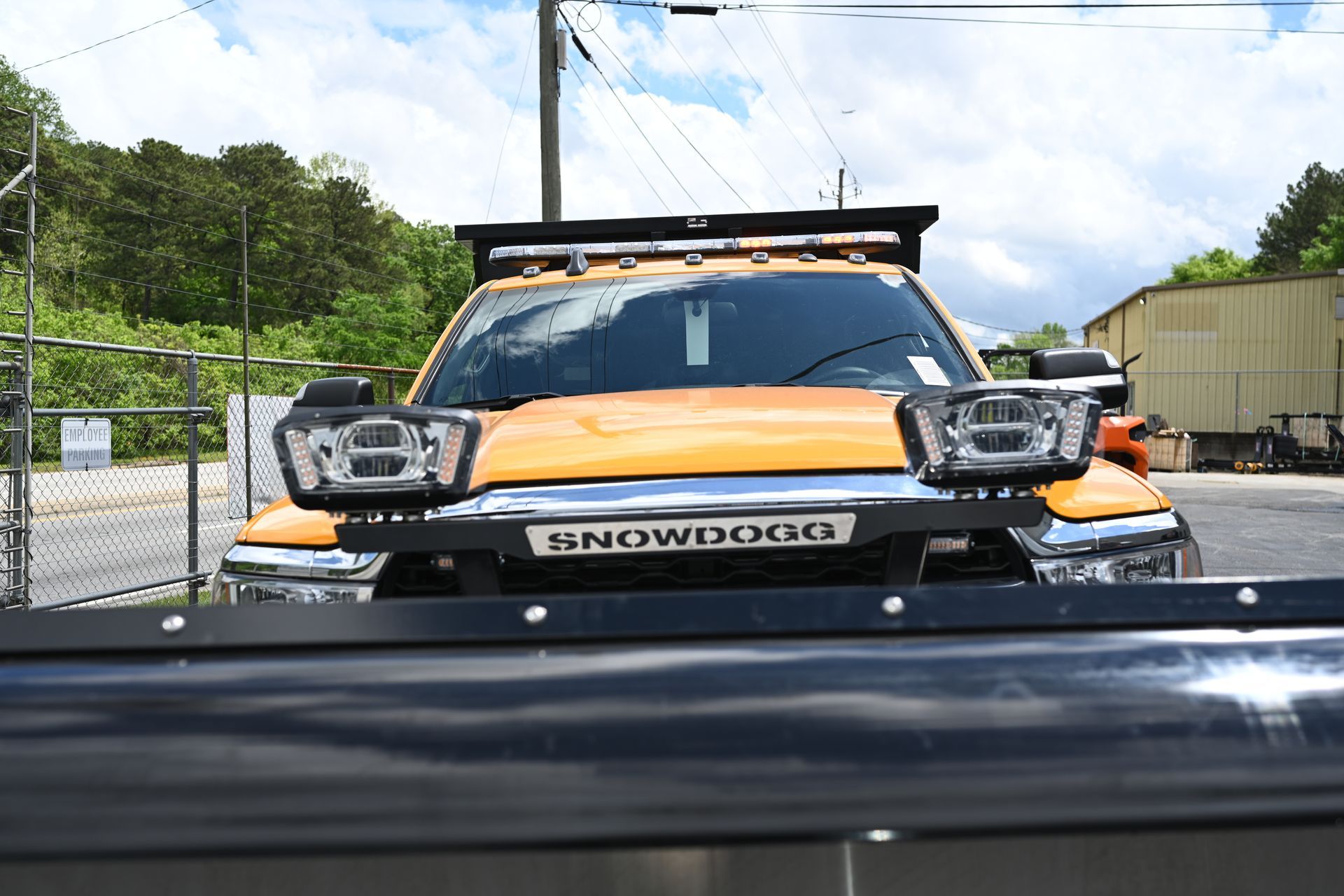 A yellow truck with a snow plow on the front is parked in a parking lot.