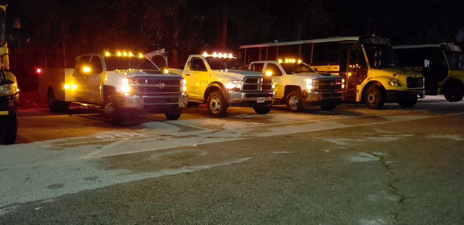 A row of trucks and buses are parked in a parking lot at night.