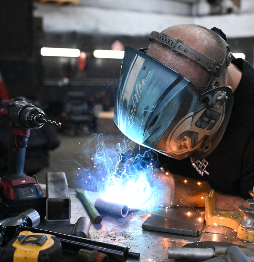A man wearing a welding mask is working on a piece of metal