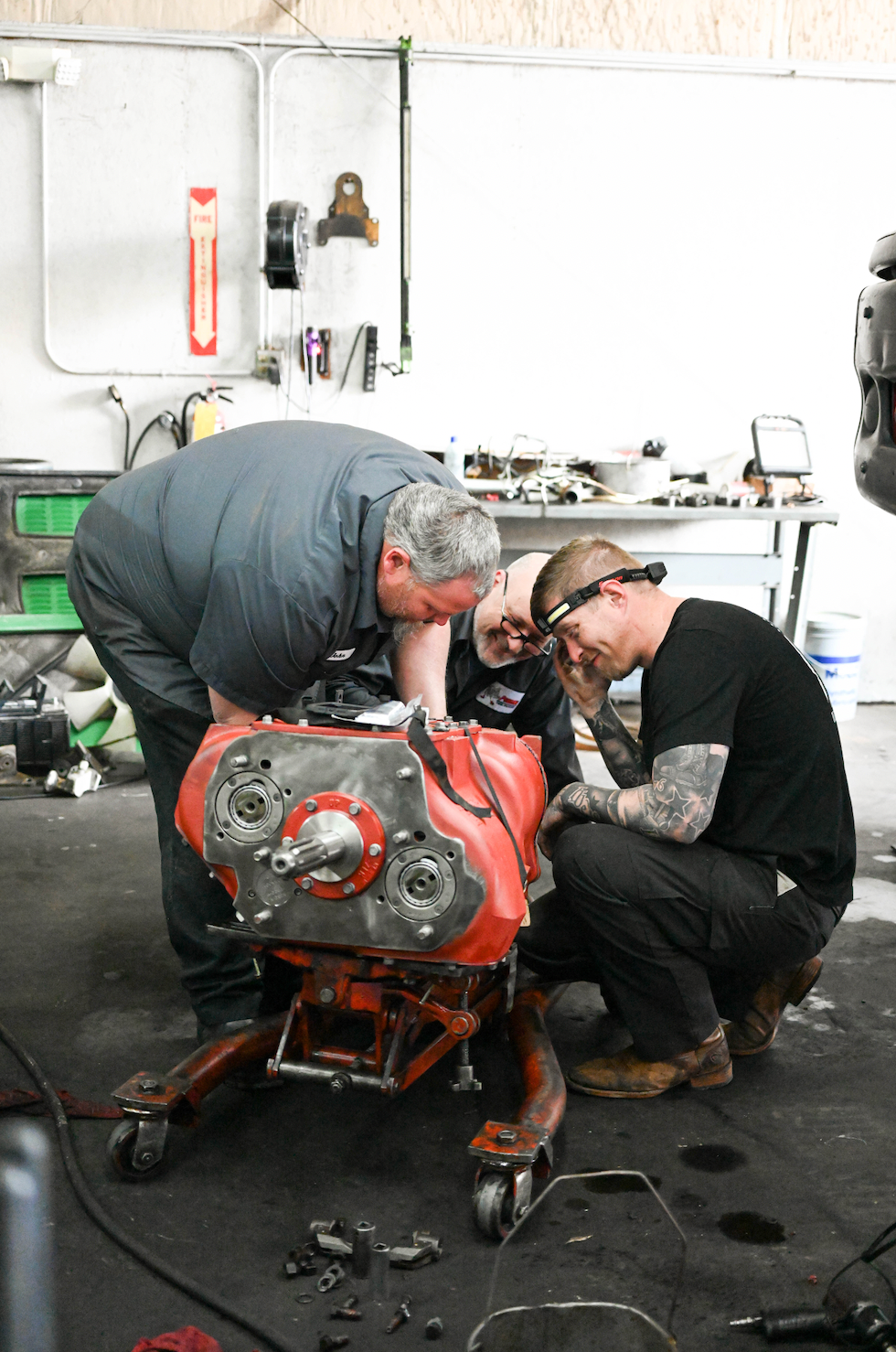 Two men are working on a red engine in a garage.