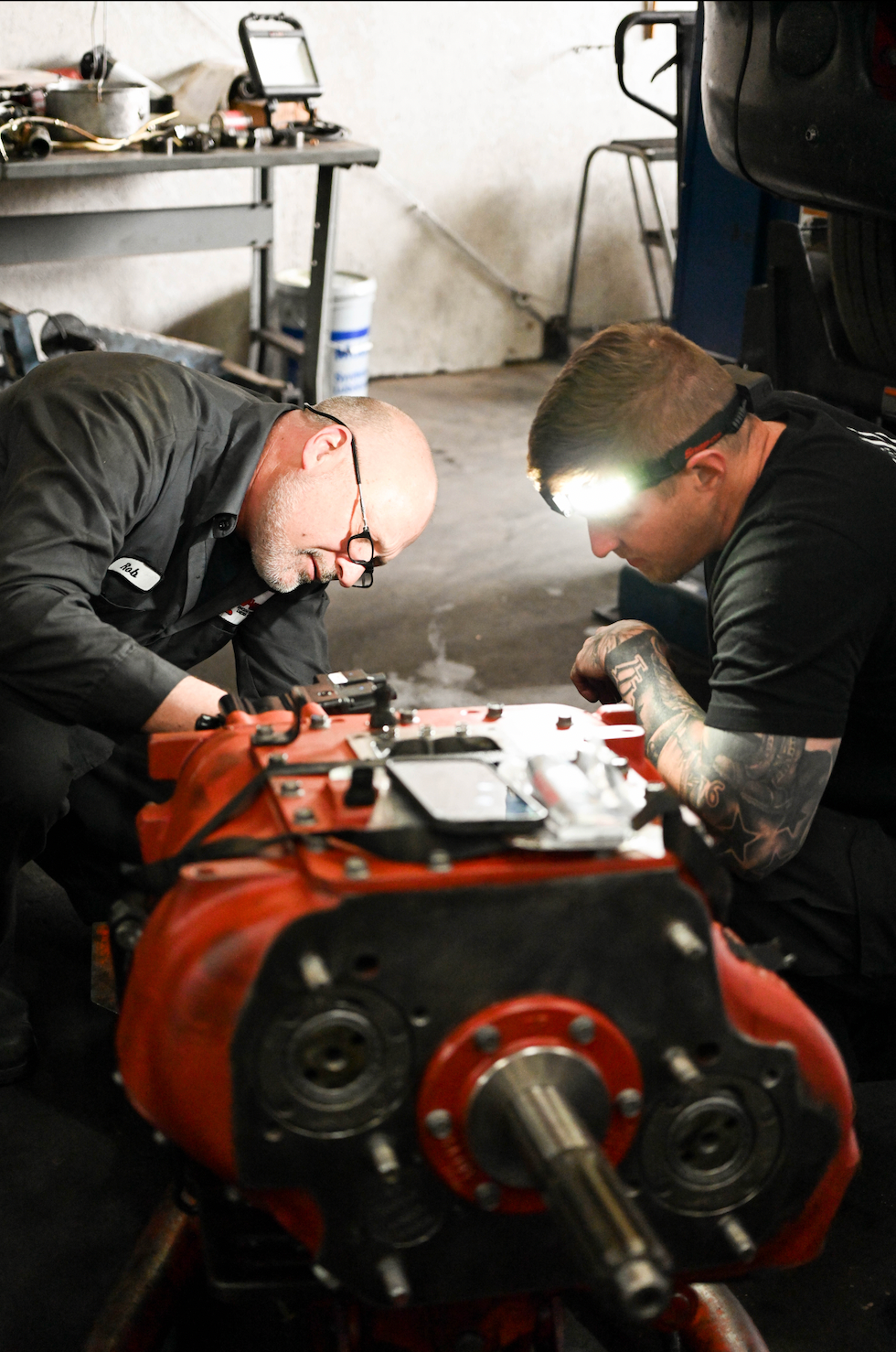 Two men are working on a red machine in a garage.