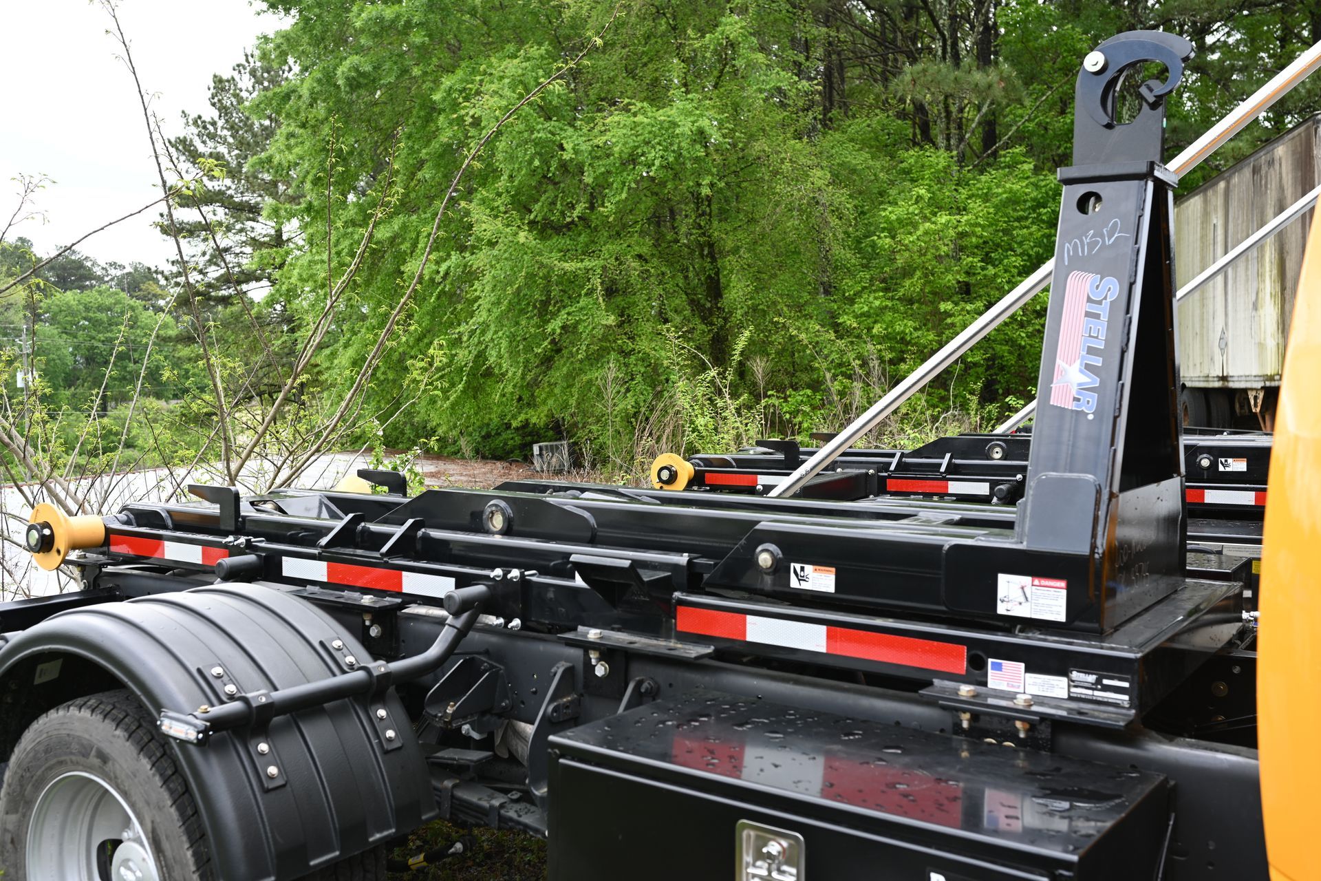 A dump truck with a container attached to it is parked in front of trees.