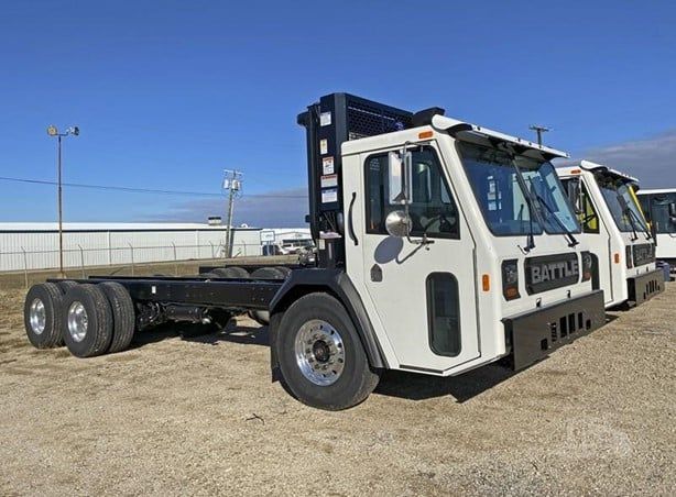 A row of white trucks are parked in a dirt field.