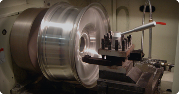 A metal car wheel being machined on a lathe; the wheel spins rapidly.