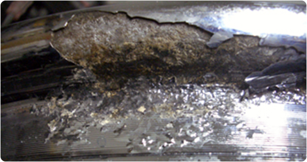 Close-up of a damaged metallic surface with extensive corrosion, flaking, and discoloration.