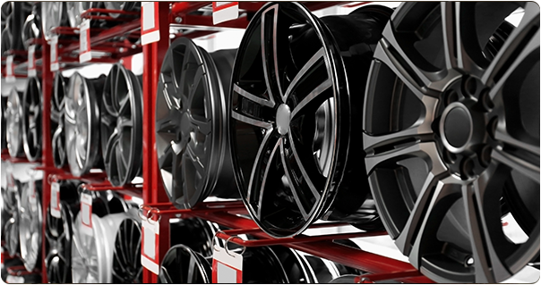 Racks of various shiny black and silver car rims on red shelving in a shop.
