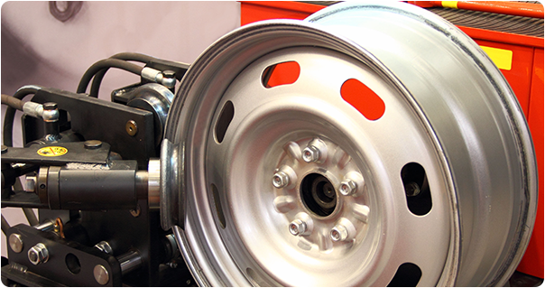 Steel wheel on a balancing machine with black arm and red accents.