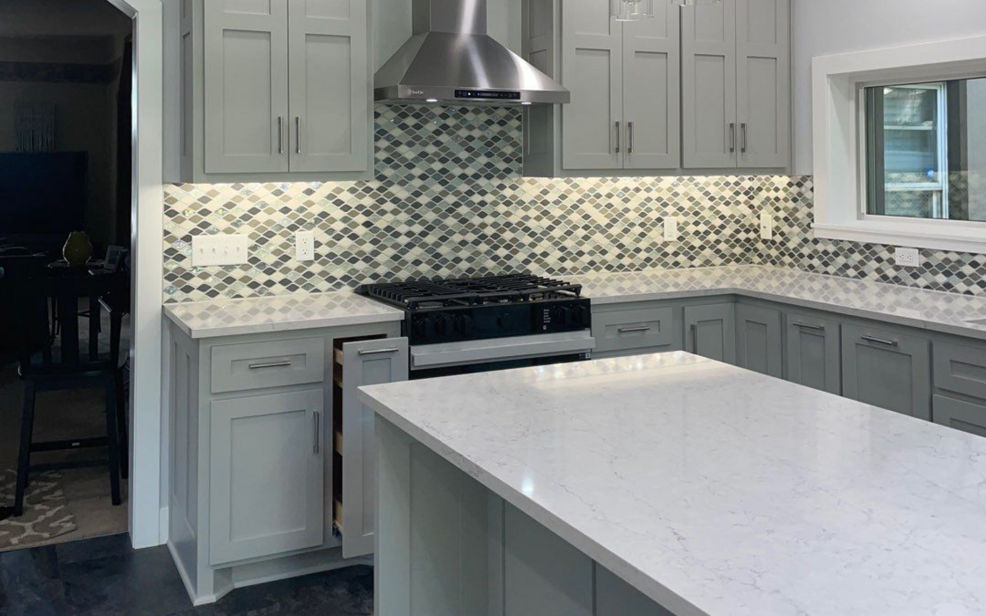Modern kitchen with a dark blue island, white cabinets, stainless steel appliances, and wooden floors.