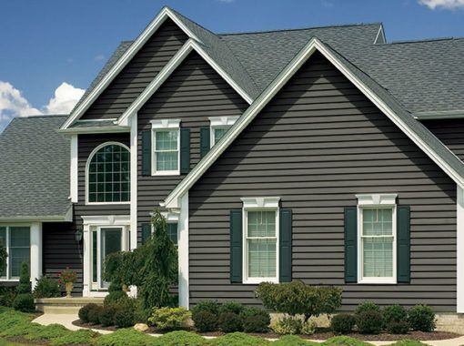 Dark gray house with white trim, green shutters, and gray roof. Landscaped front yard.