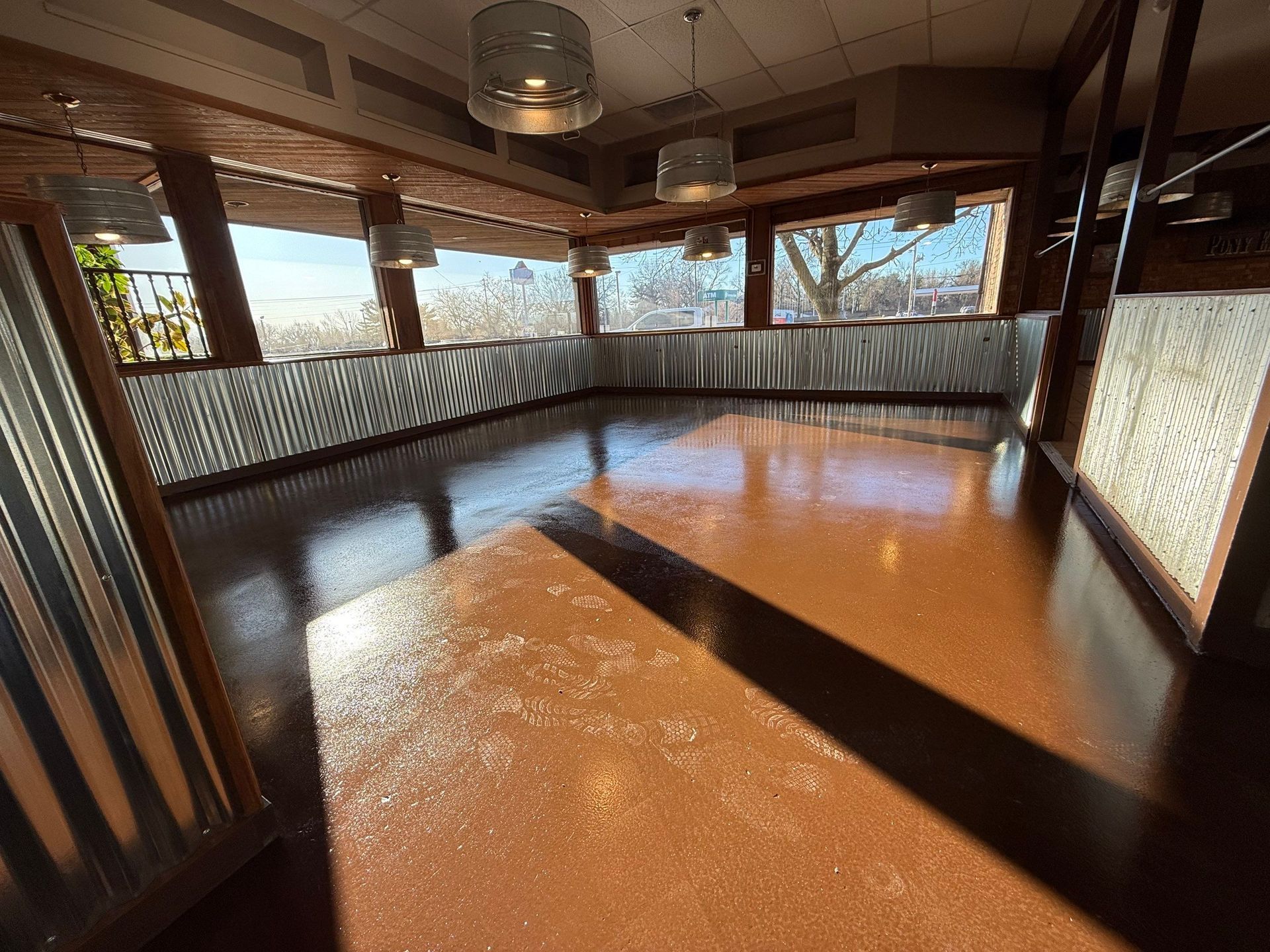 Empty dining area with shiny brown floor, windows with a view, and metal accents.
