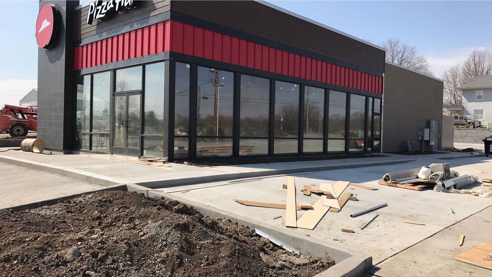 Exterior of a Pizza Hut restaurant undergoing construction; large windows, red and black accents, concrete work.