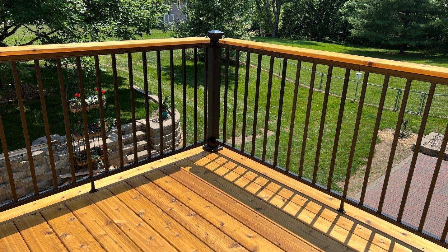Wooden deck with black metal railing and wooden handrail overlooking a green yard.