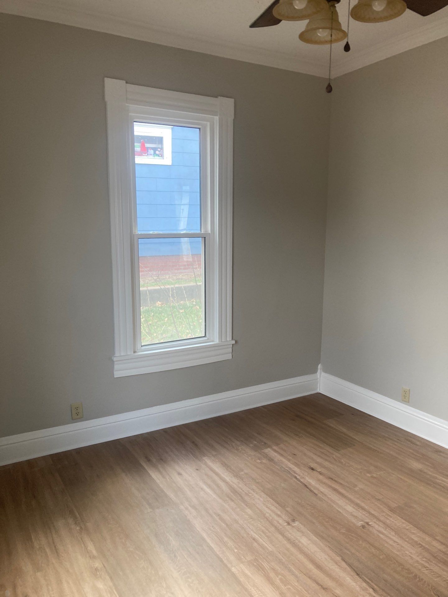 Empty room with a window, white trim, wood floors, and gray walls.