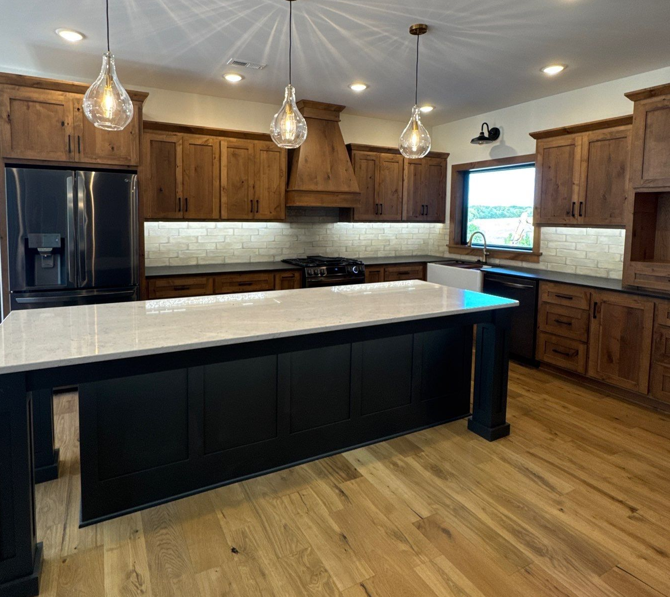 Kitchen with wooden cabinets, black island, light-colored countertop, and three hanging pendant lights.