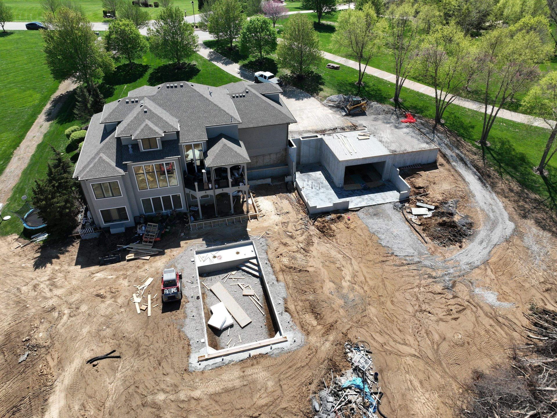 Aerial view of a large house under construction with a pool and detached structure. Brown dirt surrounds the structures.