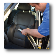 a man in a blue shirt is cleaning a car seat with a vacuum cleaner
