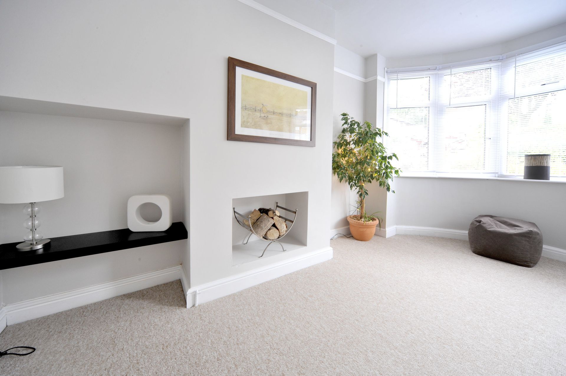 Light-filled living room with a built-in fireplace, bay window, and neutral-toned decor. There's a small plant, art, and a beanbag chair.