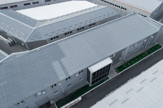 Aerial view of gray industrial warehouse buildings with metal roofs and a central entrance.