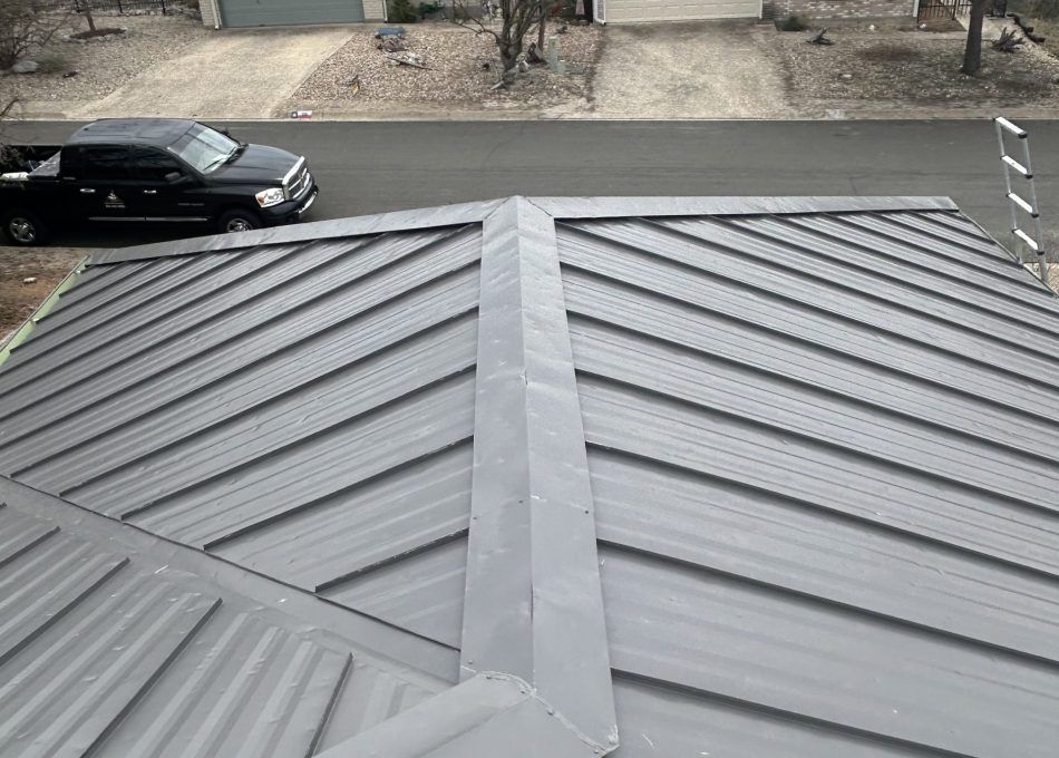 Gray metal roof with standing seams, viewed from above, with a parked black car and street in the background
