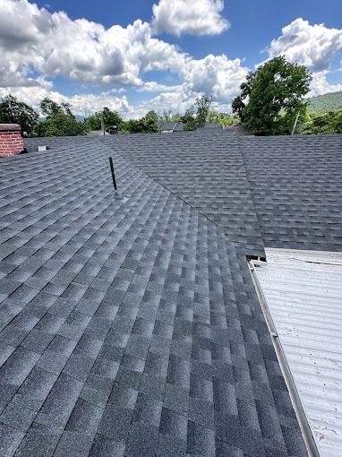 Shingled roof under a cloudy sky, with a vent pipe and a white roof section on the right