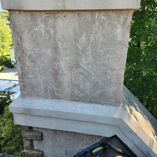 Close-up of a weathered stone chimney above a roof with trees in the background