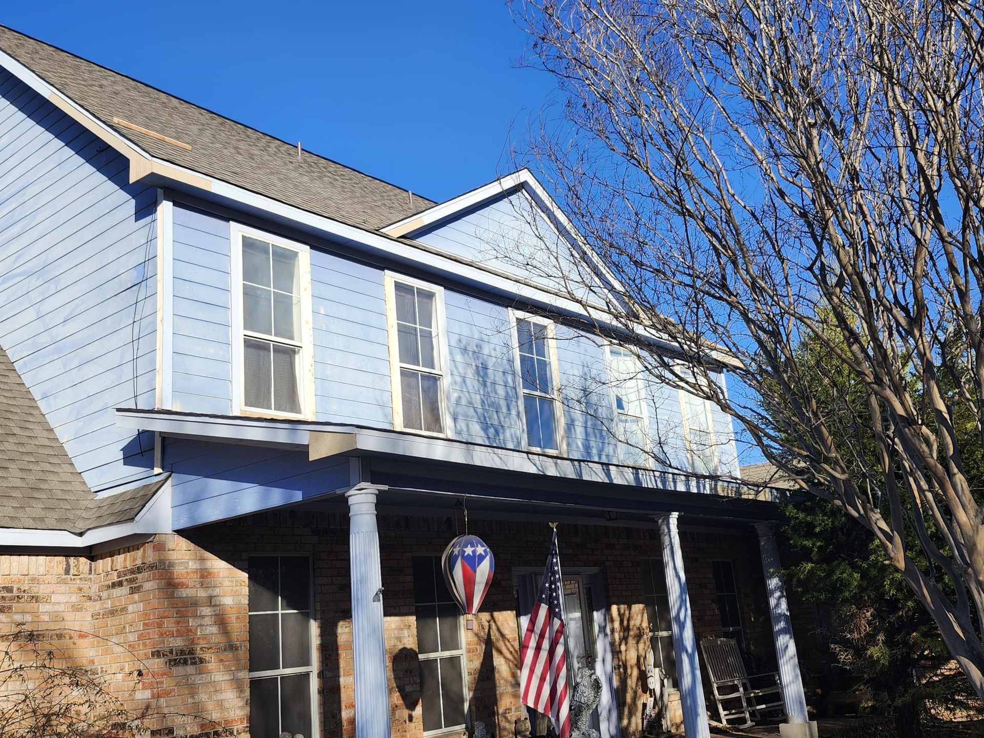 Two-story light blue house with white trim and a covered front porch in daylight