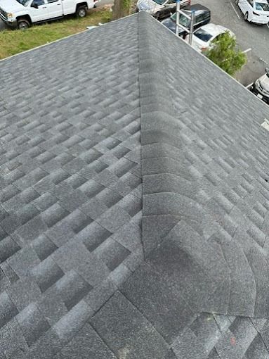 Aerial view of a gray shingled roof with a ridge line and cars visible below.