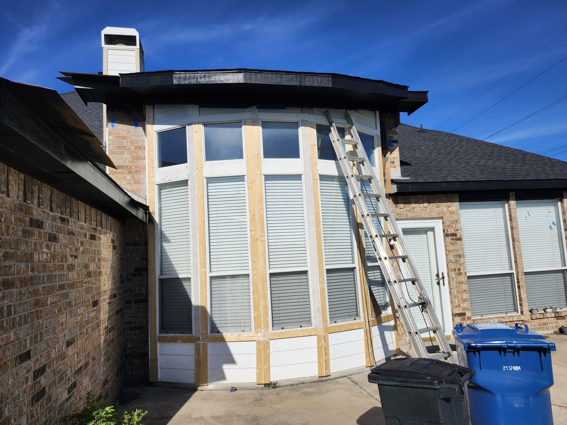 House exterior under renovation with scaffolding, ladder, and blue recycling bin under a blue sky