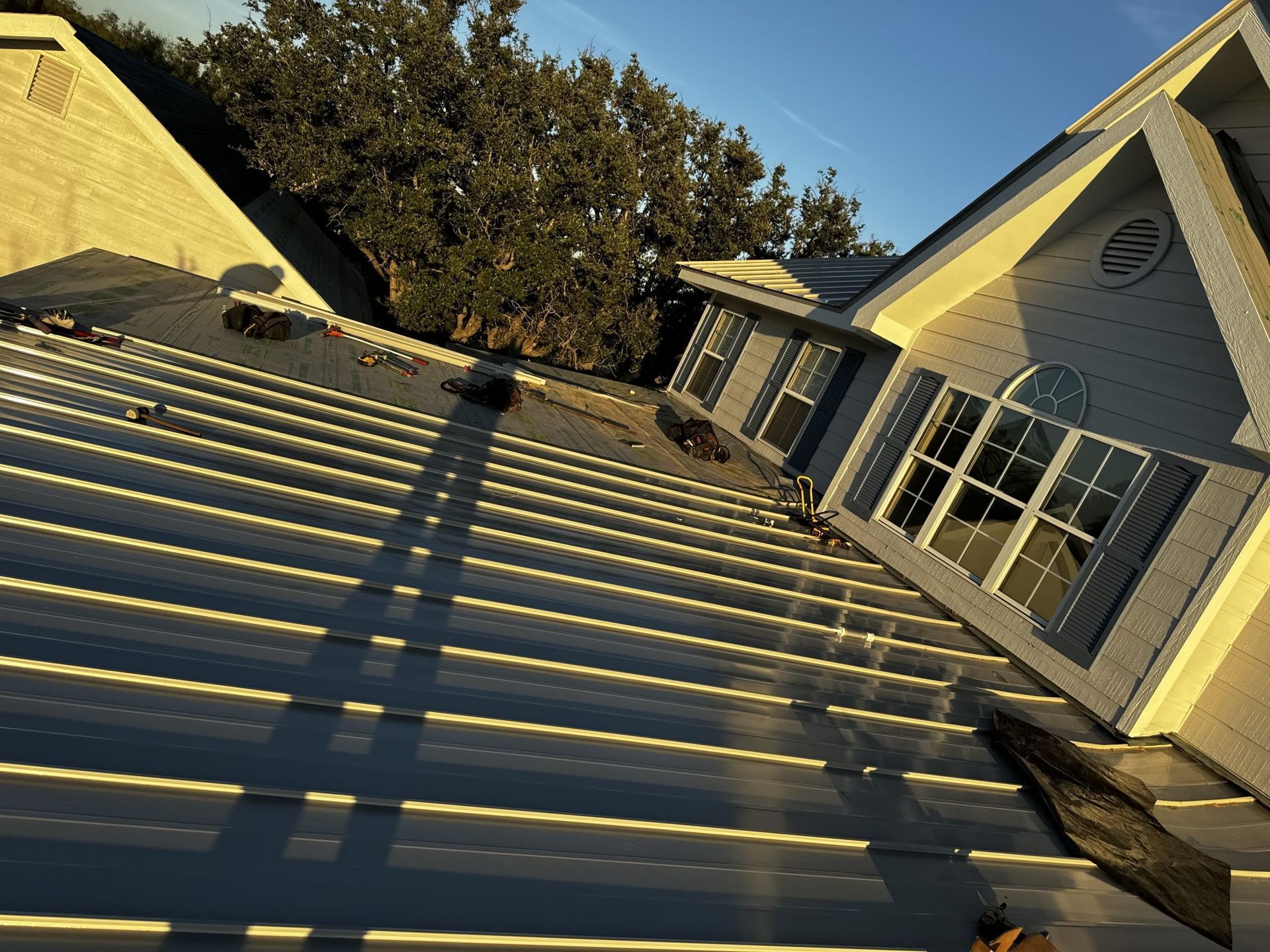 Roof with standing seam panels beside a white house, viewed at a steep diagonal angle.