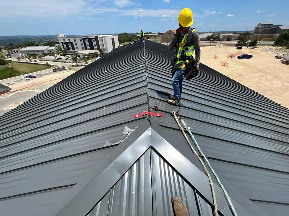 Worker in yellow hard hat on a gray metal roof during construction.