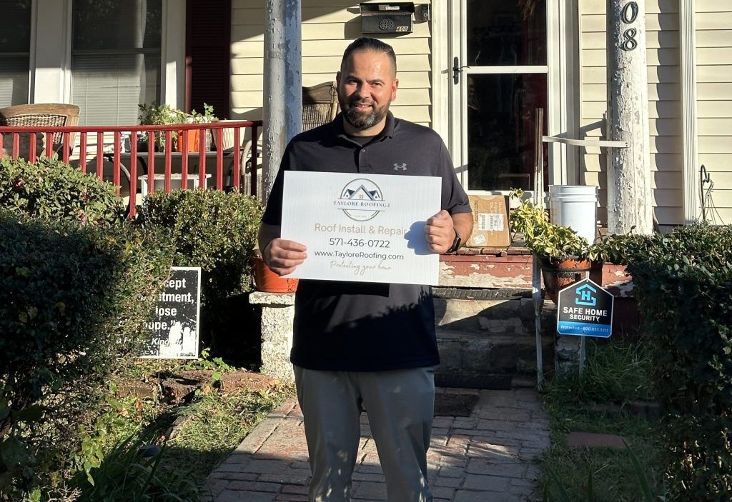 Man standing outside a house holding a sign, with shrubs and a porch in the background.