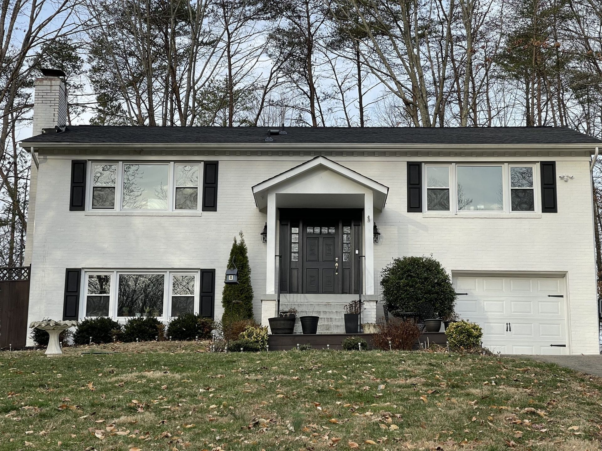 Two-story white house with black shutters, front porch, and attached garage in a suburban neighborhood