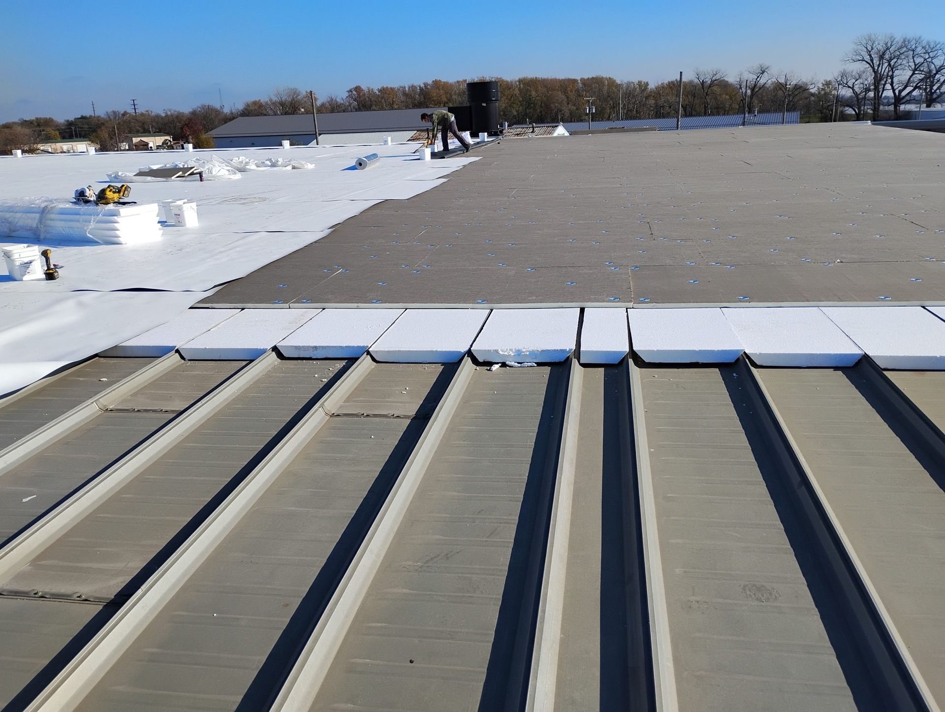 Snow-covered flat rooftop with HVAC vents and a distant worker near the edge