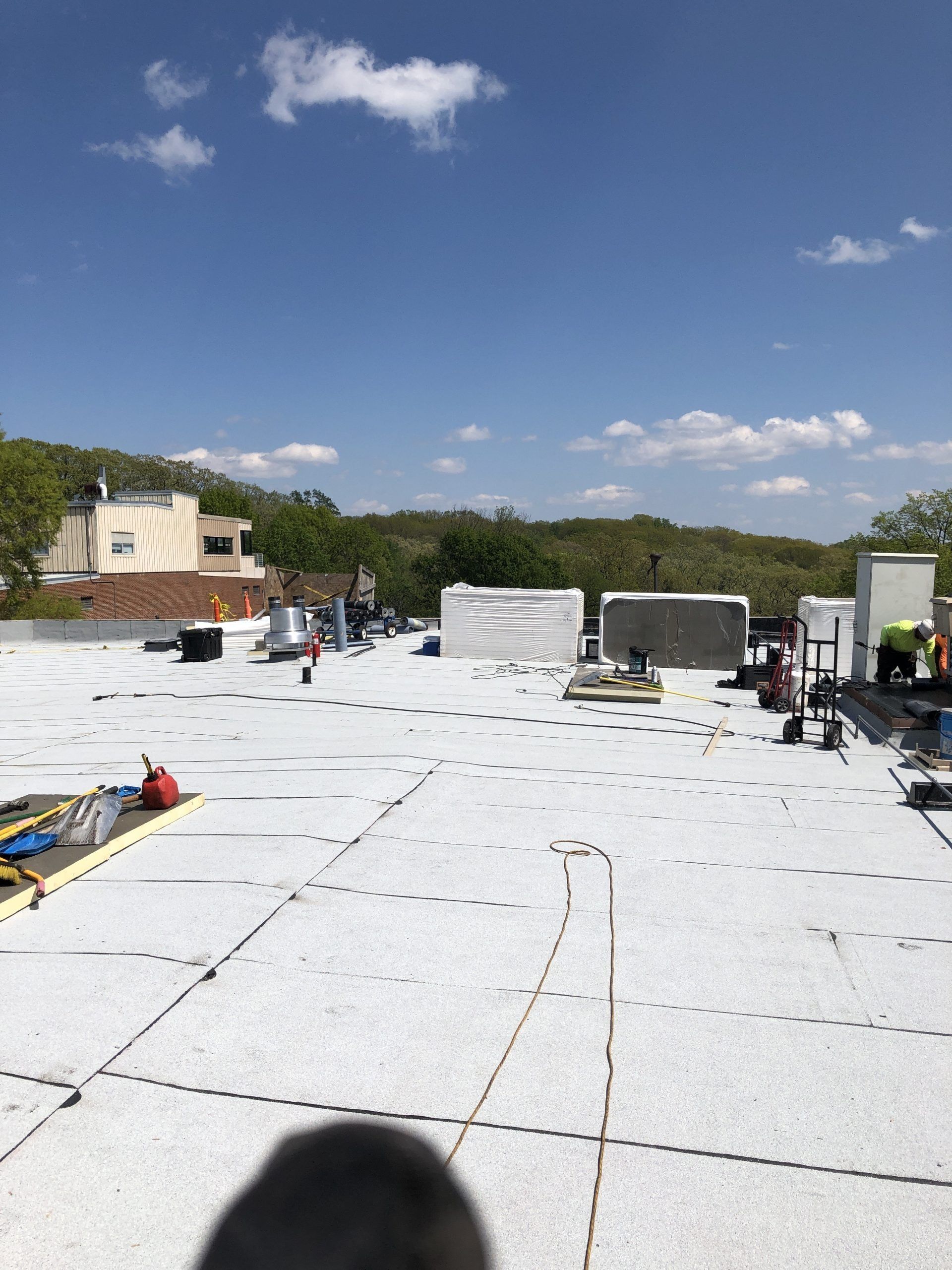 Rooftop with white roofing membrane, workers, tools, and blue sky with scattered clouds