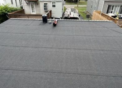 Flat gray rooftop with vents and a small ladder, viewed toward neighboring houses and a driveway.