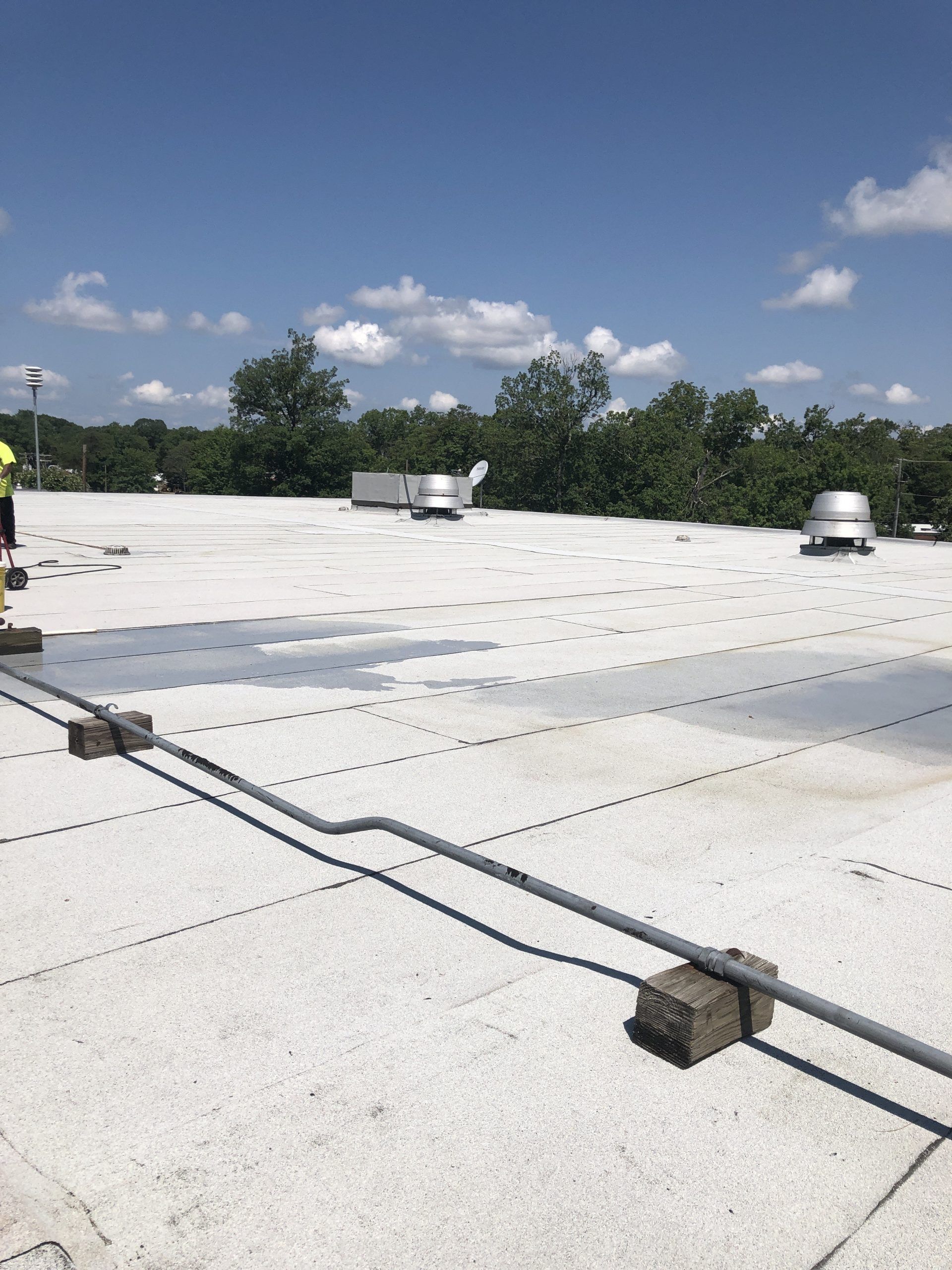 Flat white commercial roof with vents and pipes under a blue sky