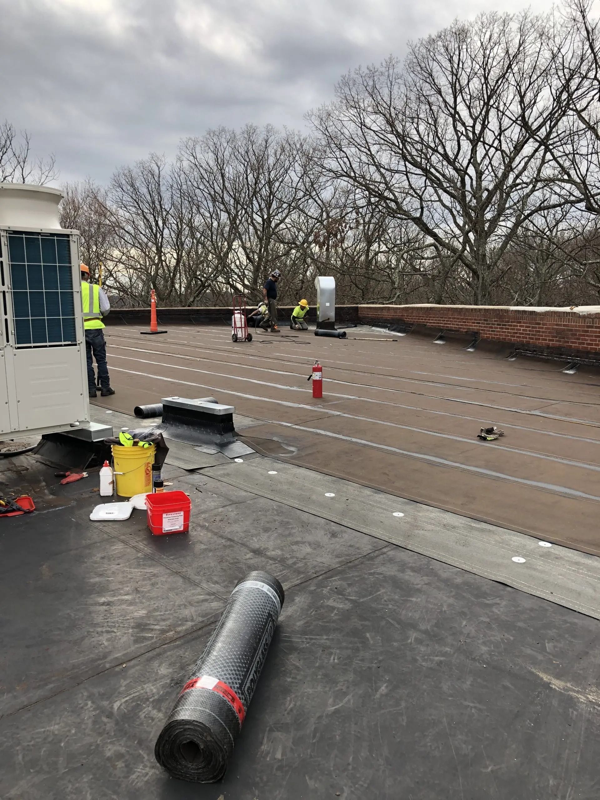 Rooftop work area with safety cones, tools, and rolled roofing material on a gray overcast day