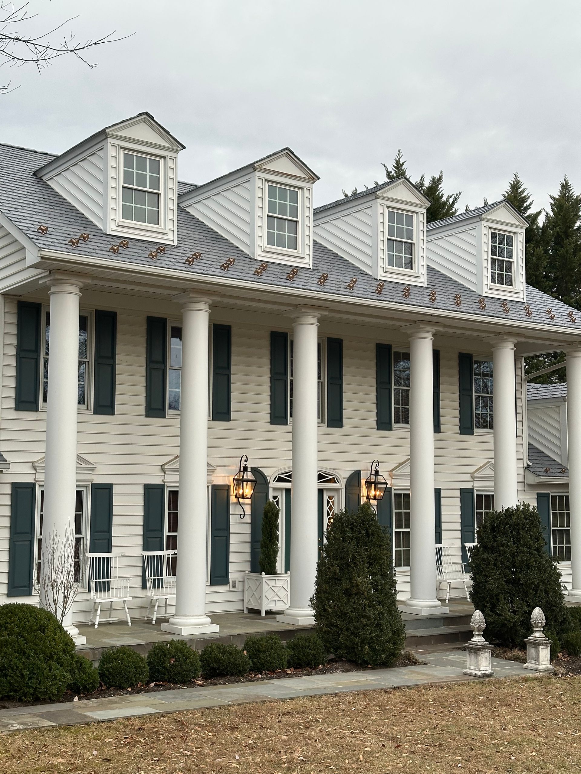 White two-story house with tall white columns, dormer windows, and a covered porch lined with lanterns