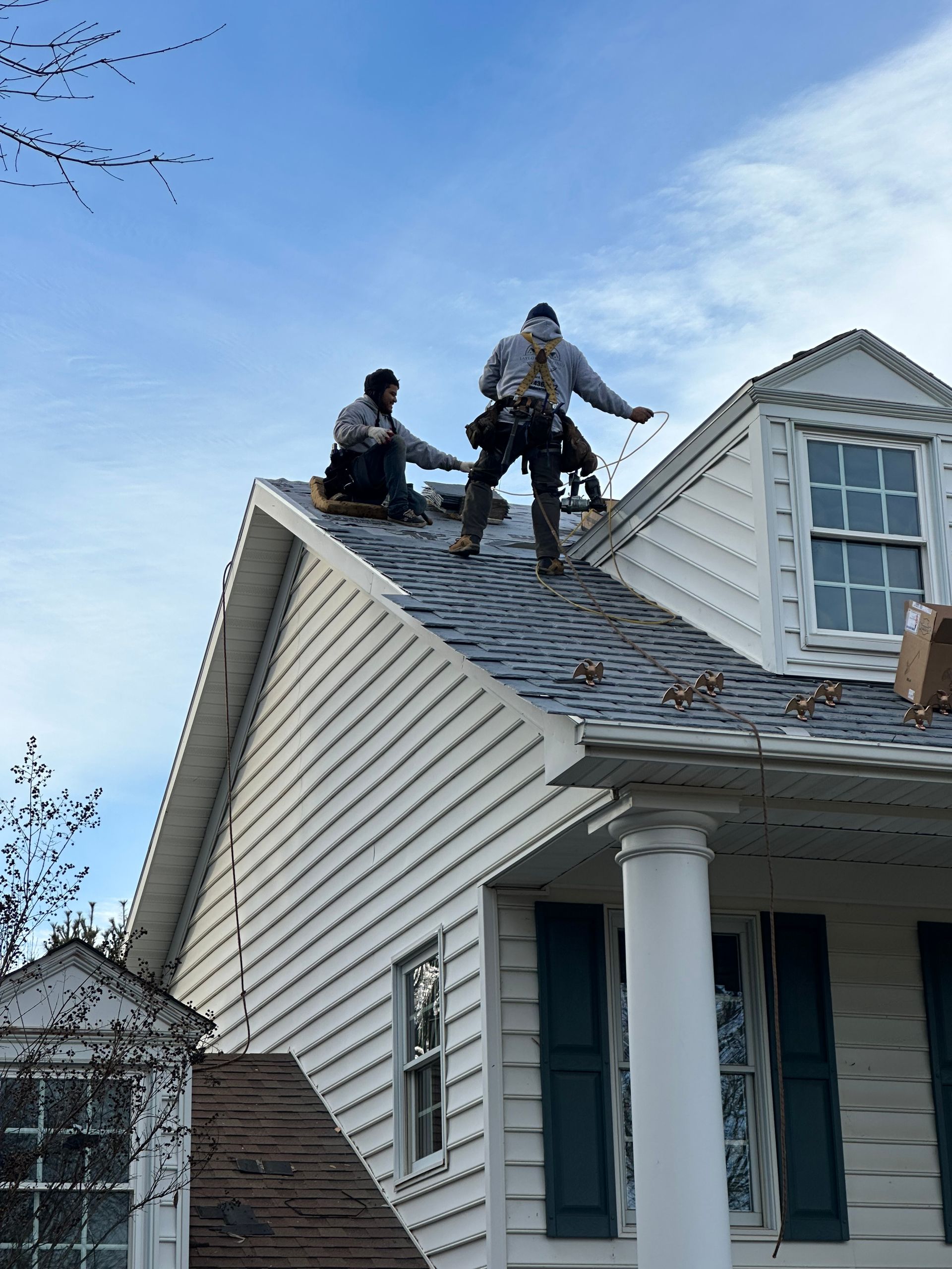 Two workers on a steep roof repairing shingles on a white house