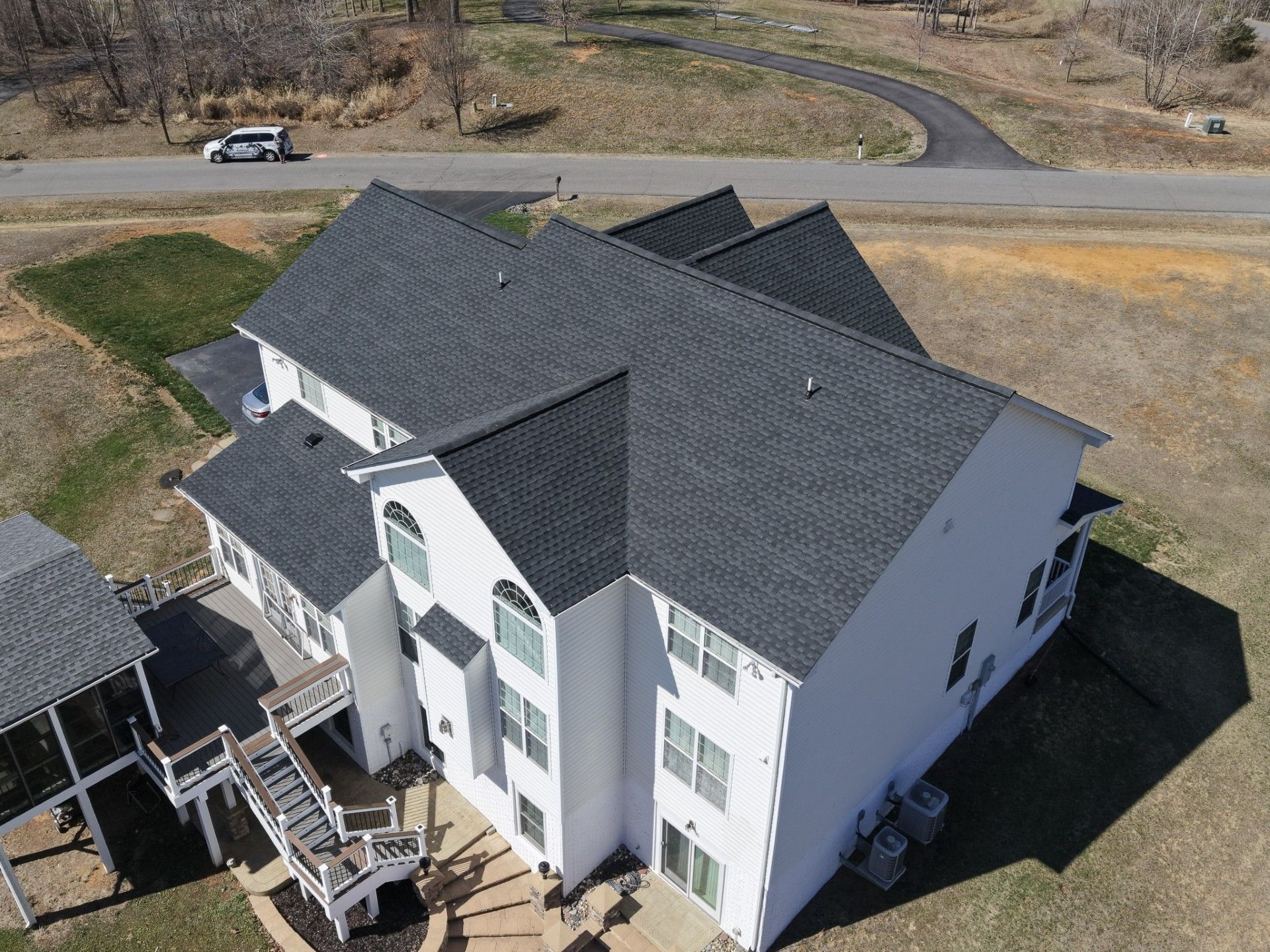 Aerial view of a white two-story house with a dark roof and deck on a rural lot