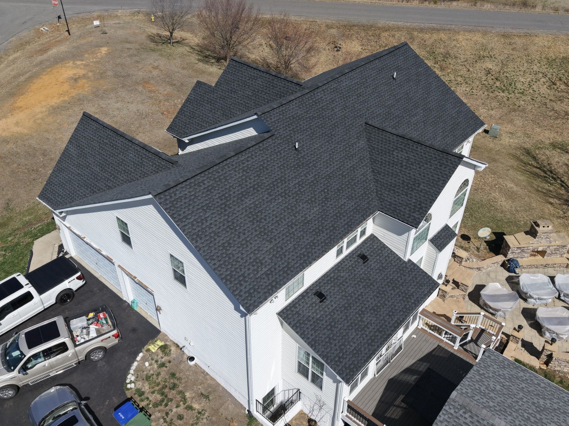 Aerial view of a white house with a dark roof, driveway, and surrounding yard under construction.