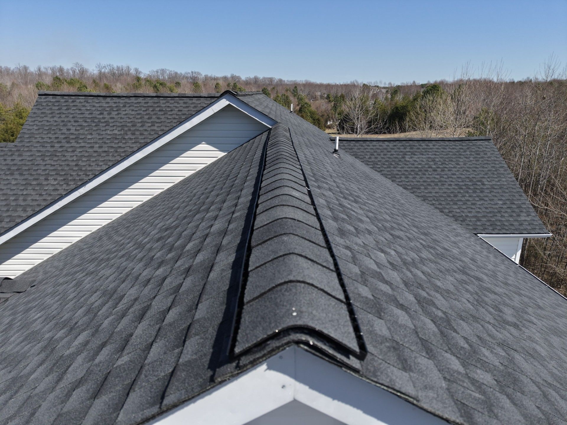 Roof ridge with dark gray shingles on a house under a clear sky