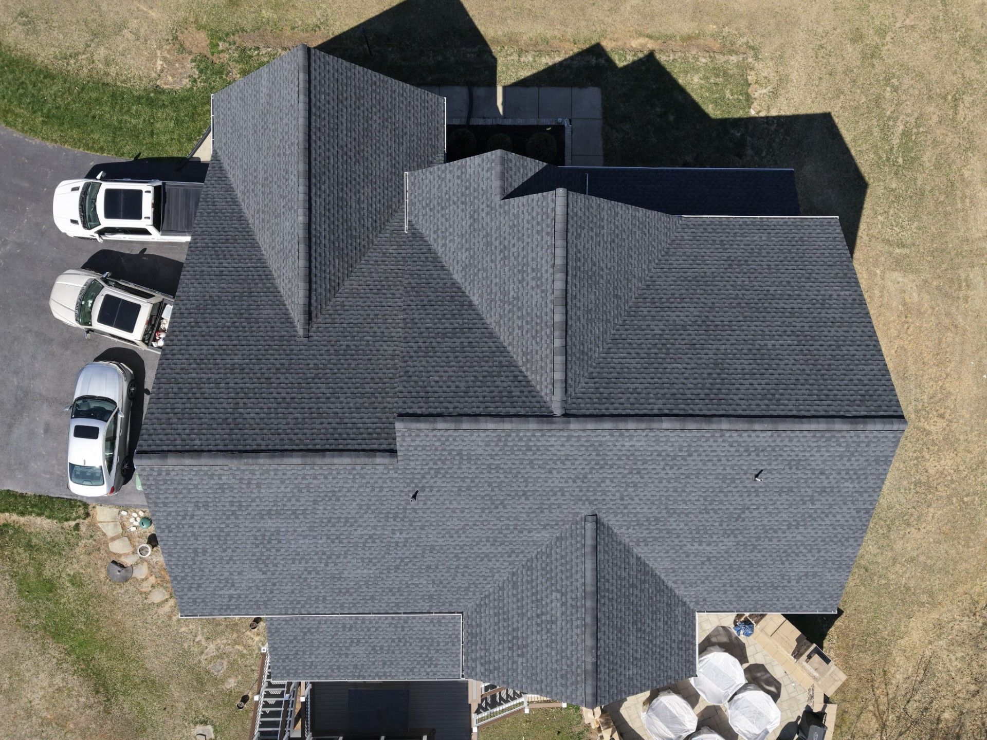 Aerial view of a large gray-shingled house with several parked cars beside it and a patchy yard.
