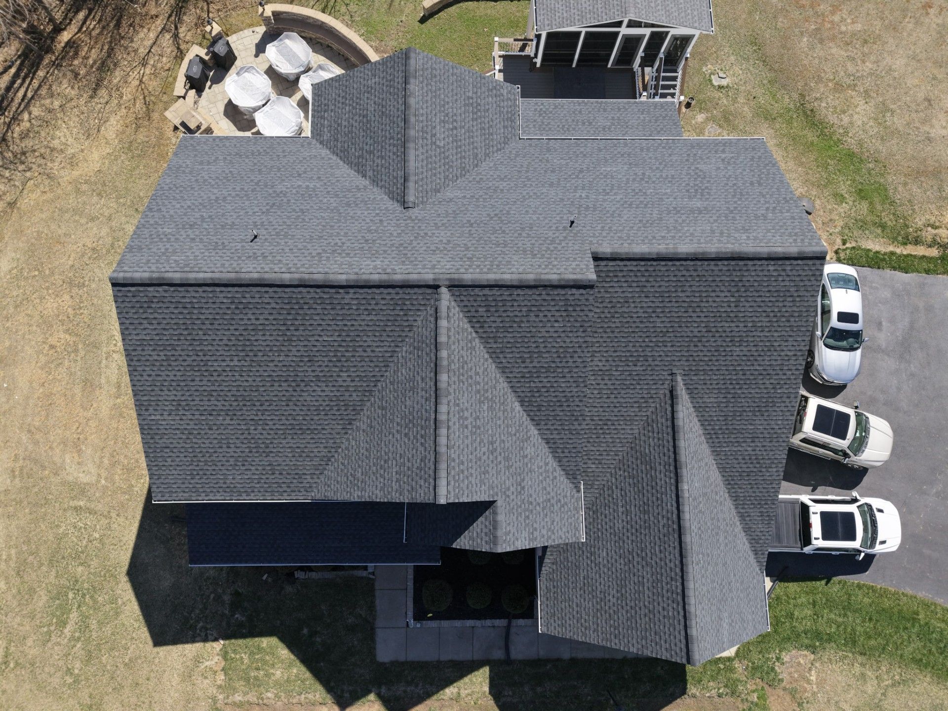 Aerial view of a gray shingled house roof with several skylights and two white vehicles nearby.
